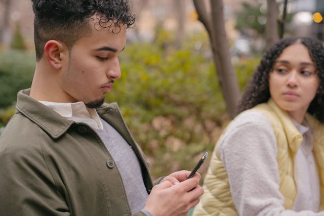 Couple assis sur un banc - La conjointe regarde d'un coin de l'oeil ce que fait son conjoint sur son téléphone - jalousie - psychothérapie paris 9