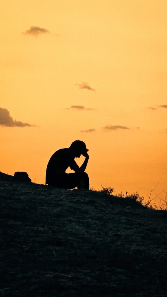 Ombre d'un homme sur fond orange, la main sur le front, pensif - deuil. Psychothérapie Paris 9