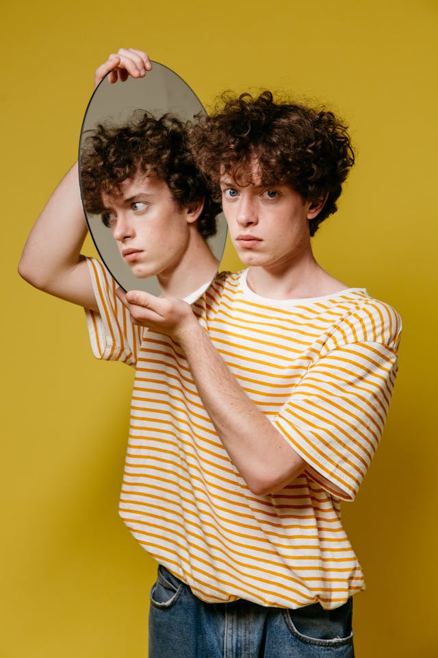 Jeune homme a un miroir qu'il tient sur le côté sans se regarder. Il est pensif - dysmorphophobie - psychothérapie Paris 9