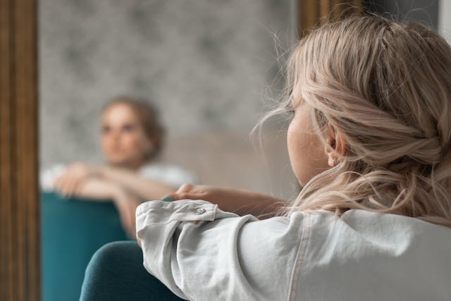 Femme dont on voit le reflet sur le miroir en flou, elle est pensive - dysmorphophobie - psychothérapie Paris 9