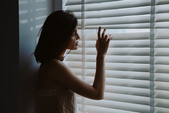 Une femme regarde par la fenêtre, d'un air inquiet - jalousie - psychothérapie Paris 9