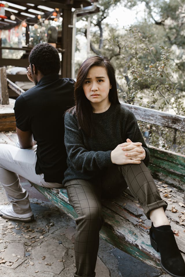 Femme triste, les mains croisés sur son genou, dos à dos avec son ex conjoint, sur un banc - deuil d'une relation - psychothérapie Paris 9