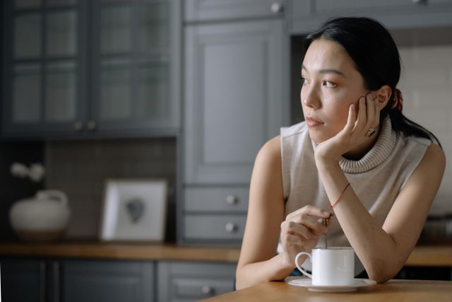Femme pensive, la main sur la joue, qui prend son café - deuil blanc - psychothérapie Paris