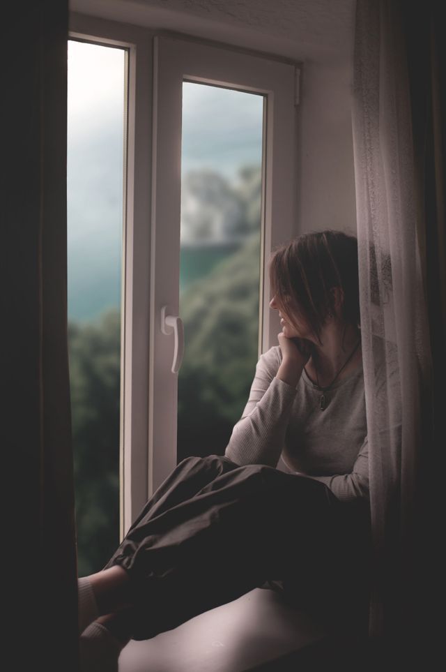 Femme, la main qui porte son menton, qui regarde par la fenêtre fermée - agoraphobie - psychothérapie Paris 9