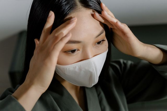 Femme qui porte un masque chirurgical et qui a les mains posées sur les tempes - nosophobie - psychothérapie Paris