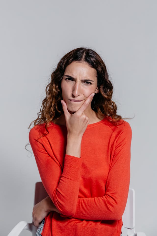 Femme debout qui fronce les sourcils, la main sur le menton et une partie des joues, inquiète - pensée intrusive - psychothérapie Paris 9