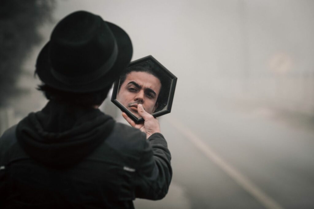 Homme qui porte un chapeau noir et de noir vêtu se regarde dans le miroir, songeur - pervers narcissique ou trouble de la personnalité narcissique - Psychothérapie Paris 9