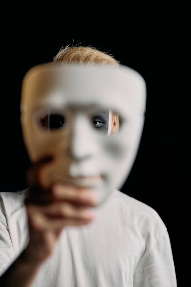 Homme maquillé de noir et blanc, qui porte à bout de main un masque blanc - PN ou TPN - Psychothérapie Paris 9