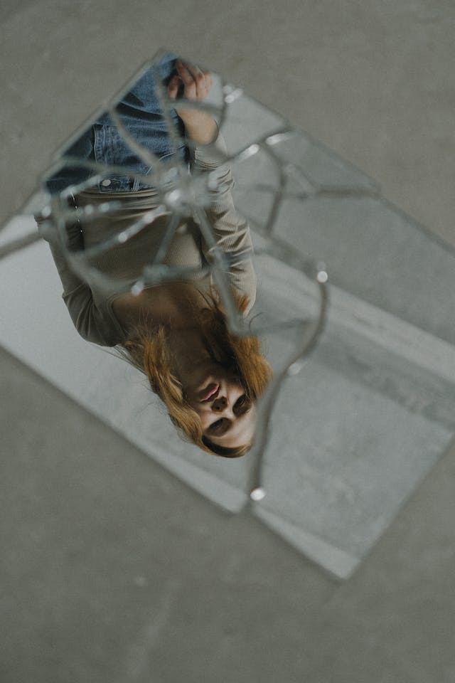 Femme qui se regarde dans un miroir cassé au sol, songeuse - pervers narcissique ou trouble de la personnalité narcissique - Psychothérapie Paris 9