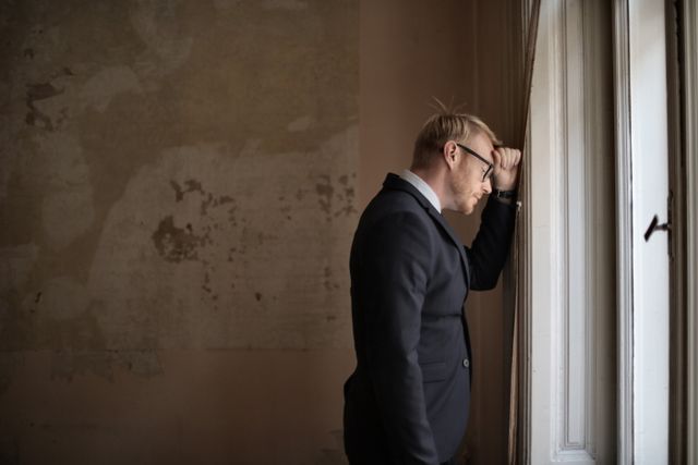 Homme en costume, la main sur le front, qui regarde par la fenêtre, désespéré - pessimisme - Psychothérapie Paris 9
