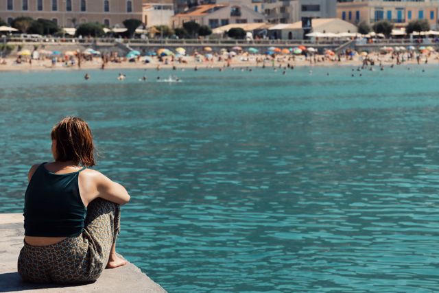 Une femme assise isolée devant la mer et la plage au loin peuplée de touristes - dépression estivale - Psychothérapie Paris 9