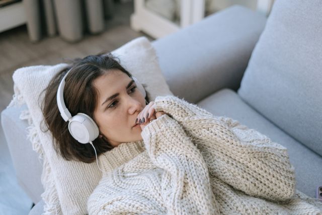 Femme allongée sur un canapé, les mains rassemblées près de sa bouche, avec un casque sur la tête - misophonie - Psychothérapie Paris 9 et Pantin