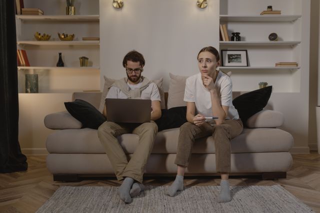 Couple assis sur un canapé. L'homme est sur l'ordinateur. La femme est pensive, la main sur le menton - TOC relationnel - Psychothérapie Paris 9 et Pantin